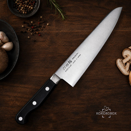 Cuchillo de chef Gyuto Kokorobox de 180mm en acero AUS-10 con mango ergonómico sobre tabla de madera con ingredientes